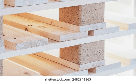 A stack of wooden pallets with a brick base. The pallets are stacked on top of each other, creating a sturdy base. Concept of strength and durability