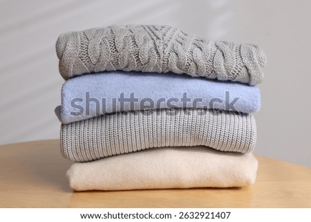 Stack of woolen sweaters on wooden table against light background, closeup