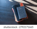 Stack of worn Bibles on a dark tabletop, lit by soft window light, evoking quiet faith, study, and reflection.