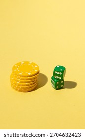 Stack of yellow poker chips and two green dice arranged on a yellow background, creating a minimalistic gambling and casino-themed composition.