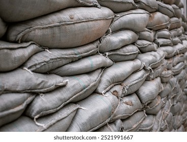 Stacked burlap bags filled with material, showcasing the texture and layers of the sacks, ideal for industrial settings and construction themes. or Sandbags for flood protection of the old military - Powered by Shutterstock