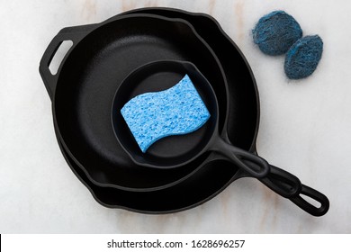 Stacked Cast Iron Skillets with Sponge and Steel Wool on Marble Countertop