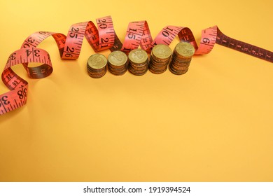 Stacked Coins And Measuring Tape On The Yellow Background.  Budget Cut Concept