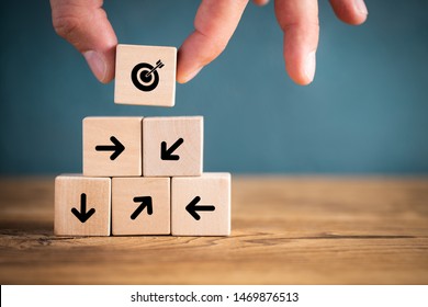 stacked cubes on wooden background with a target symbol and arrows pointing to this target symbolizing to organize a team to a common goal - Shutterstock ID 1469876513