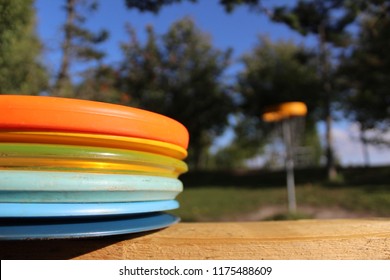 Stacked disc golf discs with blurred disc golf basket on background.