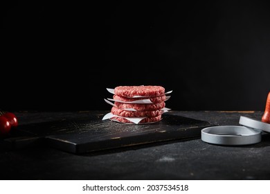 Stacked freshly made beef burger patties with patty former on a large black wooden cutting board in dim light with copyspace as a food template - Powered by Shutterstock