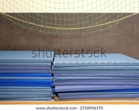 Stacked, heavily worn gym mats in an unsanitary gym. Used for floor exercises like tumbling, safety drills, and wrestling. Full of retro charm