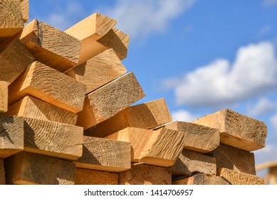 Stacked lumber on blue sky.Folded wood.Closeup wooden boards.The surface of the end of the board.Lots of planks stacked on top of each other in the warehouse.Lumber for use in construction. - Shutterstock ID 1414706957
