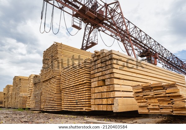 Stacked lumber\
in the warehouse of the production site against the background of a\
cantilever gantry\
crane.