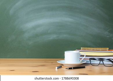 Stacked notebooks and cup of coffee on wooden school desk with a green chalkboard. The blank blackboard in the background for copyspace
