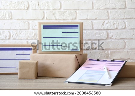 Stacked packages of different sizes wrapped in craft paper with shipping labels. Bunch of parcel boxes on the table. Close up, copy space for text, white brick wall background.