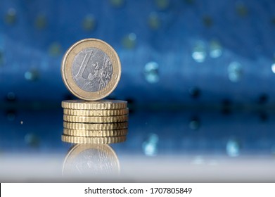 Stacked photos of one Euro coin standing on a pile of cents, mirrored and in front on a blue background