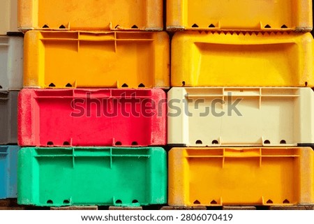 Stacked plastic fish crates in various colors, including yellow, red, green, and cream, arranged neatly for storage in a warehouse setting