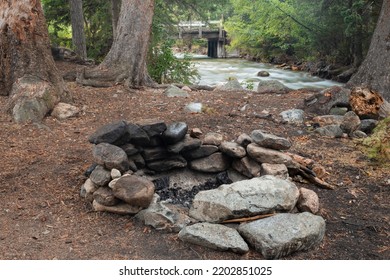 Stacked Rock Wall Fire Pit At Makeshift Camp Site In Forest Woods To Use As Campground For Camping With Safety To Prevent Forest Fire In Tree Clearing Near River And Bridge