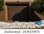 Stacked sandbags securing a garage entrance against potential water damage during flood season. Property protection, flood defense, and emergency preparedness in urban environments