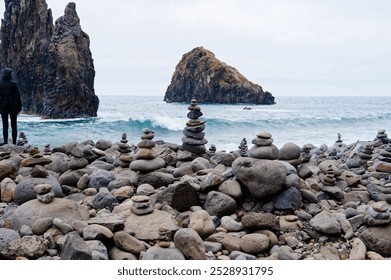 Stacked stones on Ilhéus da Janela beach with towering rock formations and ocean waves in the background. - Powered by Shutterstock