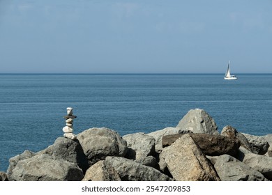 Stacked stones on rocky shore with a sailboat in the distance on a clear day - Powered by Shutterstock