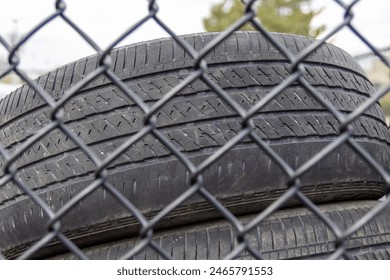 Stacked used tires - behind chain-link fence - under cloudy sky. Taken in Toronto, Canada. - Powered by Shutterstock