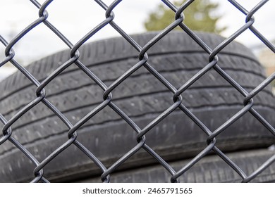 Stacked used tires - behind chain-link fence - under cloudy sky. Taken in Toronto, Canada. - Powered by Shutterstock