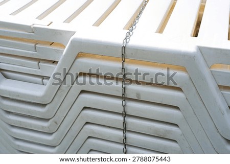 Stacked White Plastic Chairs Interlinked with a Chain, Illustrating Storage and Organization in a Compact Outdoor Setting