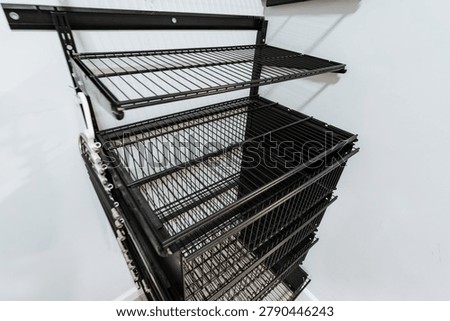 Stacked wire storage baskets made of dark metal with grid panels and reinforced frames sit on a clean white surface, showing an organized industrial storage solution with orderly shelving and depth