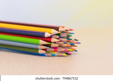Stacked wooden coloured pencils on sunny background.