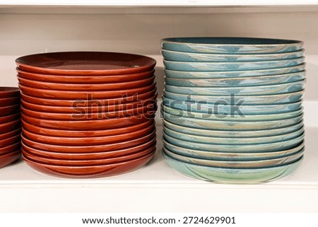 Stacking ceramic plates in vibrant red and turquoise colors, showcasing artisan pottery and handmade dinnerware on a white shelf