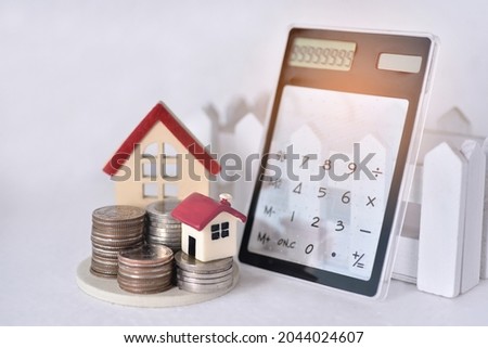 Stacking coins with the big and small red roof house and the trasparent calculator indicating the numeric lean against the  sunrise