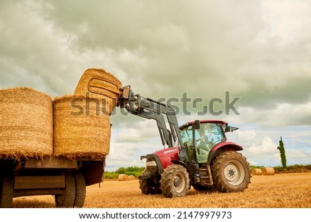 Stacking those hay bales. Shot of a farmer stacking hale bales with a tractor on his farm.