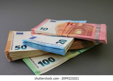 Stacks of 10, 20, 50 and 100 euro banknotes, tied with rubber band and lying one on one, isolated on a grey background. Euro money. Close up view.