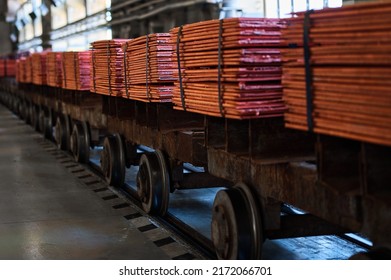 Stacks of cathode copper sheets tied with ribbons on rail carriages in light warehouse at metal refinery plant closeup - Shutterstock ID 2172066701