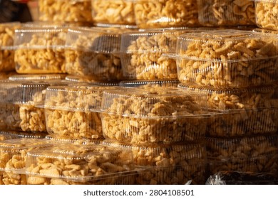 Stacks of clear plastic containers filled with golden-brown, crispy snacks. Sunlight highlights the crunchy texture and warm tones. Ideal for food blogs, packaging design, or market scenes