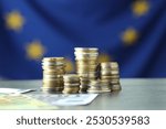 Stacks of coins and euro banknotes on grey table