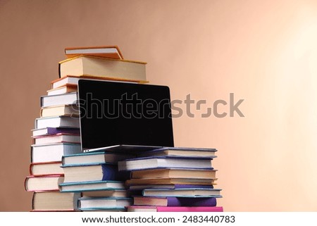 Stacks of colorful books and laptop on light brown background, space for text