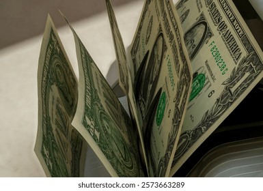 Stacks of dollar bills are processed by a currency counting machine in a financial office. The setting reflects a bustling environment typical of economic activity.
