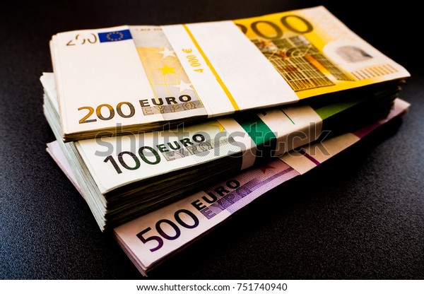 Stacks of Euro notes on a dark desk in five\
hundred, two hundreds and one\
hundreds.