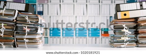 Stacks of\
files and paperwork in the office and bookshelves on the\
background: management and archive\
concept