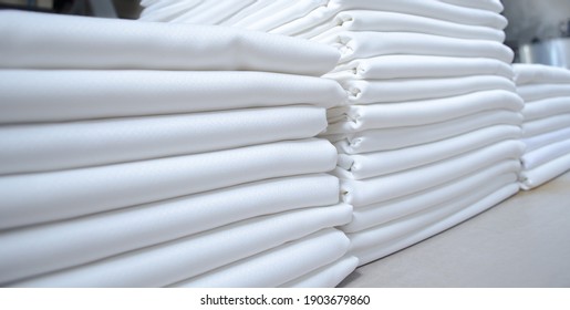 Stacks of folded white fabrics or sheets in a laundry. Cleaning service for institutions and industries.