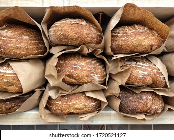 Stacks of freshly-baked loaves of sourdough bread with crusty tops dusted in flour, wrapped up in brown paper bags on bakery shelf - Shutterstock ID 1720521127