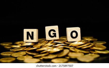 Stacks Of Gold Coins With The Letters NGO (Non Governmental Organizations) On A Wooden Cube. NGO Or Non-governmental Organization Written.                        