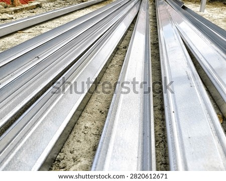 Stacks of light steel channel frames (baja ringan) on a construction site ground, prepared for building framework.
