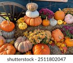 Stacks of orange pumpkins and mums sit on bales of hay against a cart with a large wooden spoked wheel