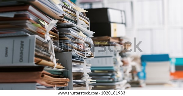 Stacks of paperwork\
and files in the office: work overload, files management and\
administration concept