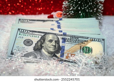 Stacks of US Dollar Bills with Festive Christmas Decorations, Santa Claus Figurine, and a Red Holiday Background - Powered by Shutterstock