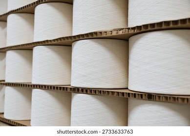 Stacks of white cotton and polyester yarn bobbins wrapped in stretch film on wooden pallets ready for shipment in a textile warehouse.