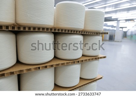 Stacks of white cotton and polyester yarn bobbins wrapped in stretch film on wooden pallets ready for shipment in a textile warehouse.