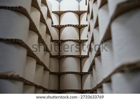 Stacks of white cotton and polyester yarn bobbins wrapped in stretch film on wooden pallets ready for shipment in a textile warehouse.