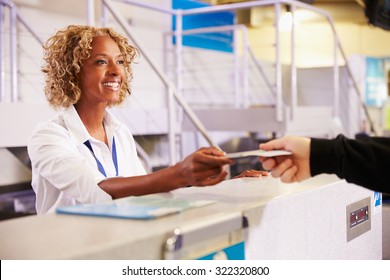 Staff At Airport Check In Desk Handing Ticket To Passenger