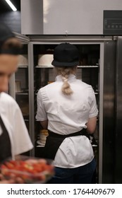 The Staff Of The Chefs In The Kitchen Of The Restaurant Or Cafe. The Girl Looks In The Refrigerator In Which There Are Cakes.