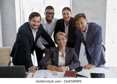 Staff In Formal Suits Pose For Corporate Picture, Gathered Together In Modern Office Board Room. Middle-aged Female Boss, Subordinates Smile Look At Camera. Teamwork, Business Success, Unity Concept